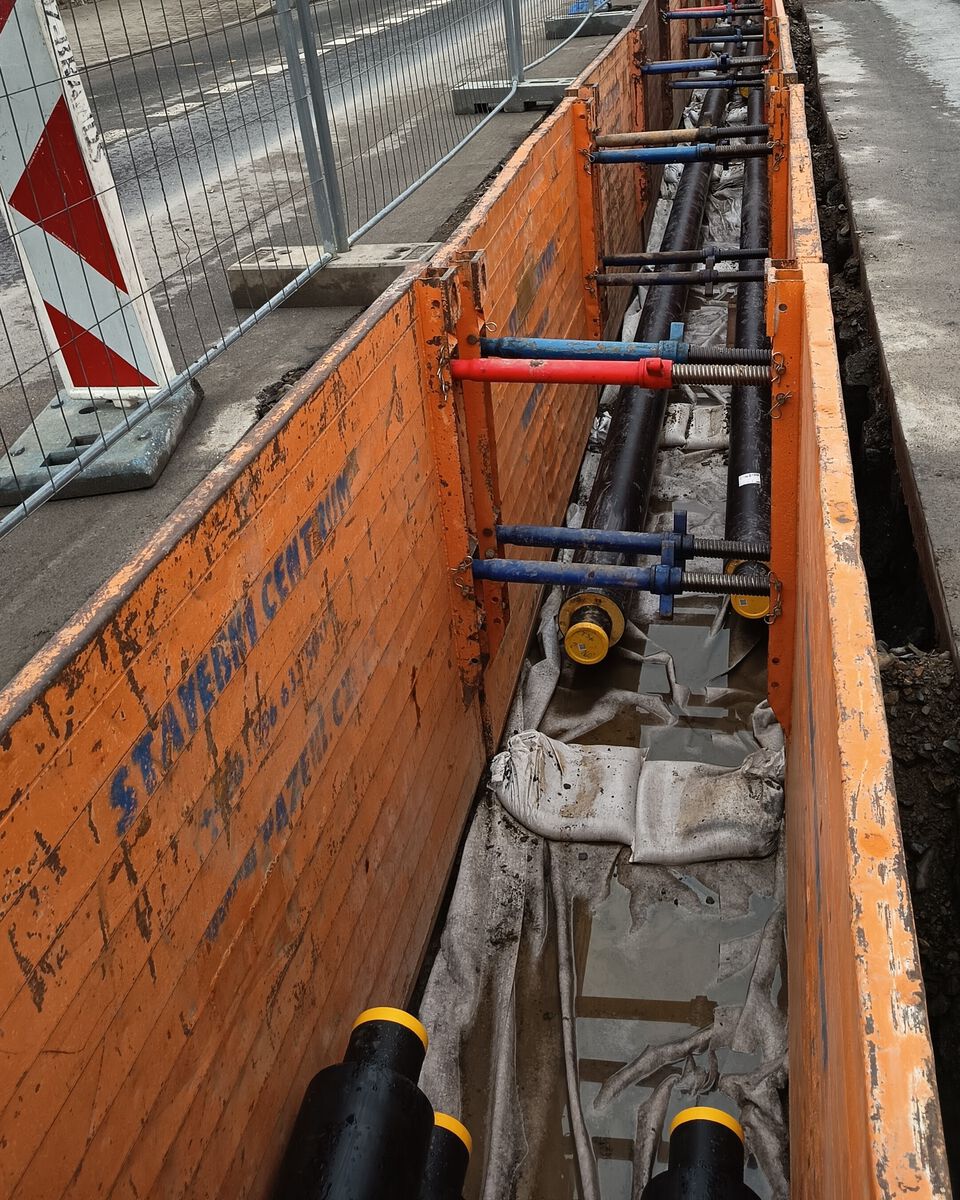 Pažící box s nápisem STAVEBNÍ CENTRUM a rozpěry nad dvojicí potrubí ve výkopu